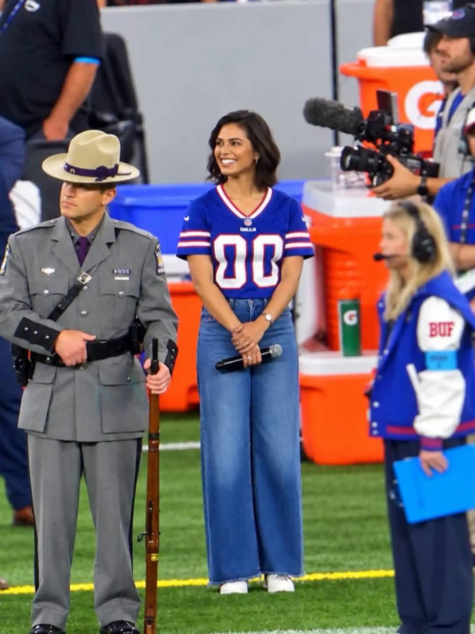 Auli'i Cravalho on the field in a Buffalo Bills jersey, mic in hand, before singing the national anthem at Highmark Stadium.